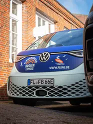 Der Küstenlimo-Bulli von vorne mit Logo und blauer und mitfarbener Beklebung.