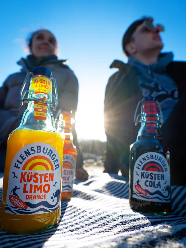 2 Küstenlimos stehen vor 2 Menschen, während die Sonne auf die Flaschen strahlt.