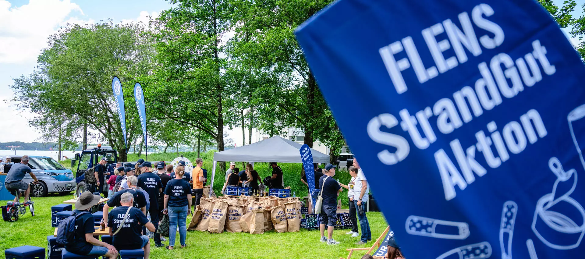 Menschenmenge, die sich nach der Strandreinigungsaktion bei einem Glücksrad und mit FLENS vergnügt.