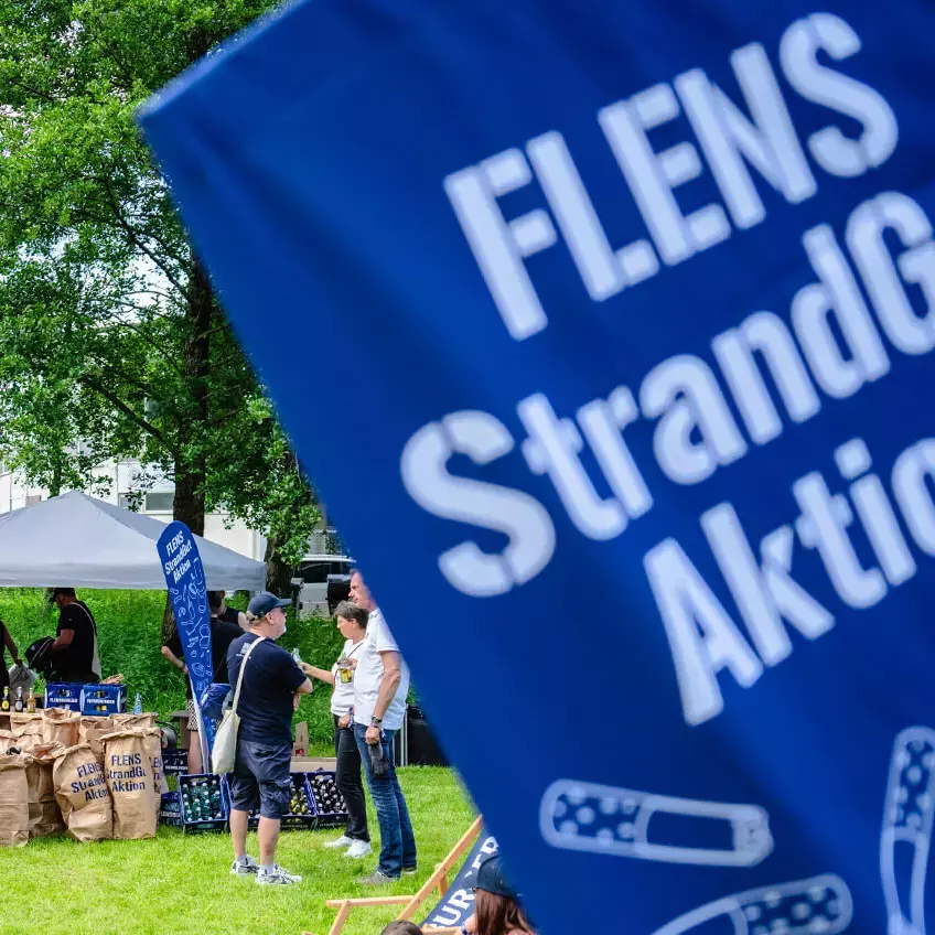 Menschenmenge, die sich nach der Strandreinigungsaktion bei einem Glücksrad und mit FLENS vergnügt.