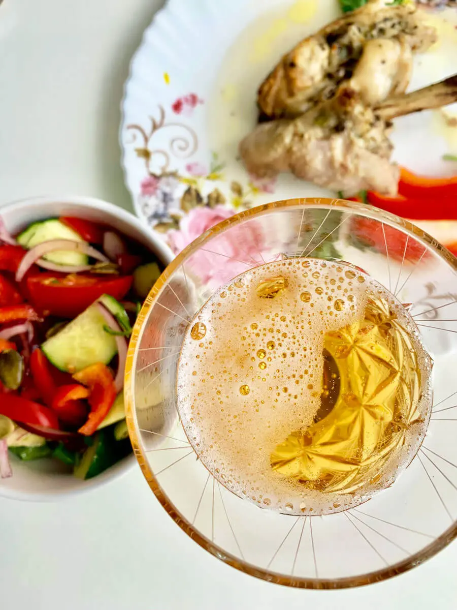 Draufsicht auf Bierglas mit Schaum, bunter Tomaten-Gurkensalat und gebratenem Hähnchen auf Teller.