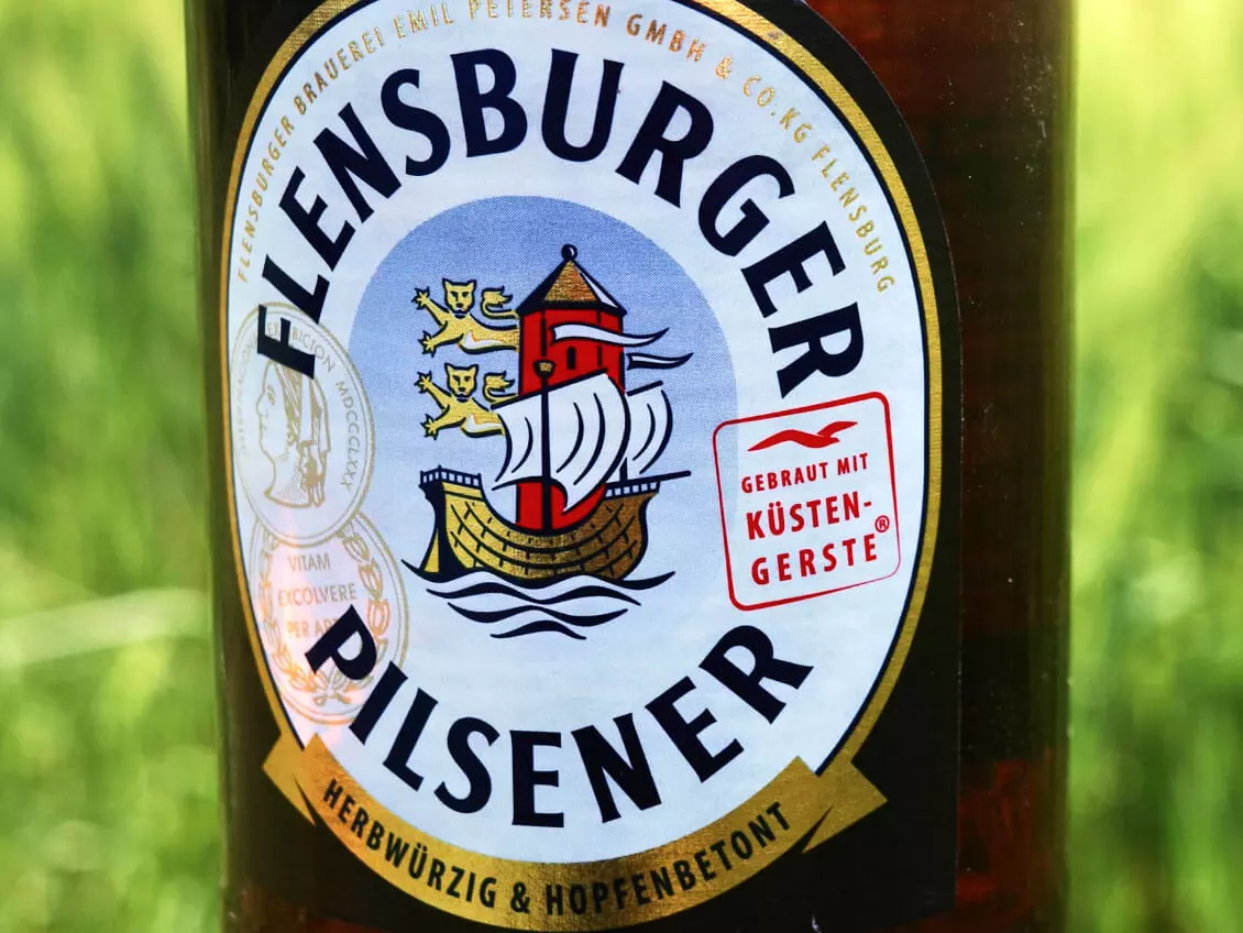 Etikett vom Flensburger Pilsener im Anschnitt vor einer grünen Wiese.