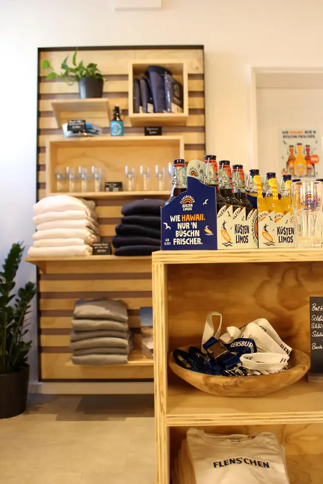 FLENS Merch und Küstenlimos in den Regalen und auf einer Mittelkonsole aus Holz im Plop-Shop.