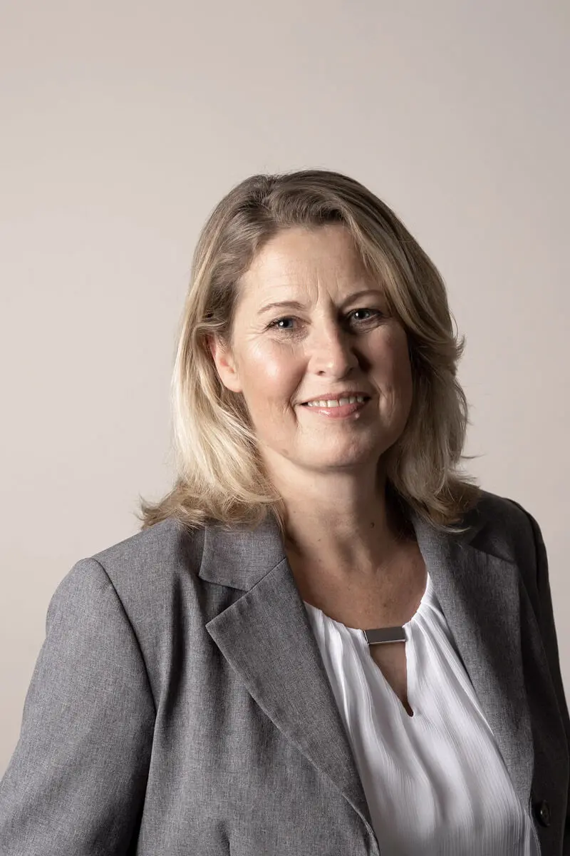 Portrait von Veronika Warmers in grauem Blazer und weißer Bluse vor neutralem Hintergrund.