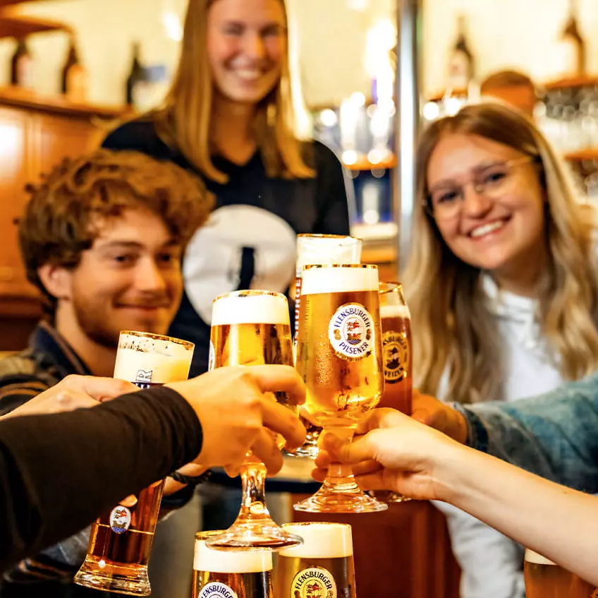 Freudige Gäste im Salon der Flensburger Brauerei, die mit Biergläsern anstoßen.