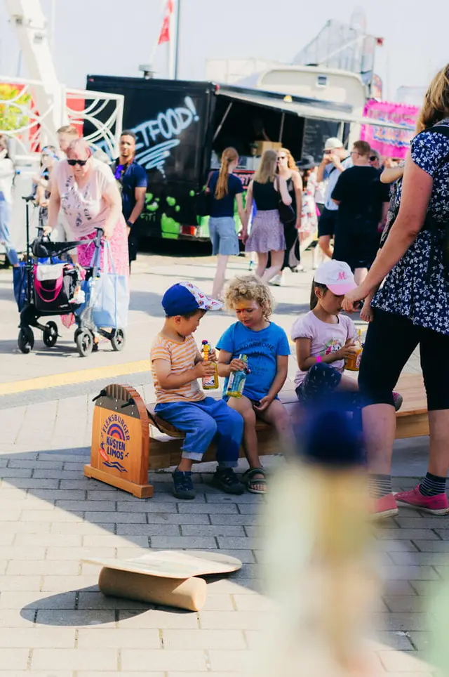 Kinder genießen Küstenlimos auf einem Balance-Board bei der Kieler Woche 2025; Food-Truck im Hintergrund.