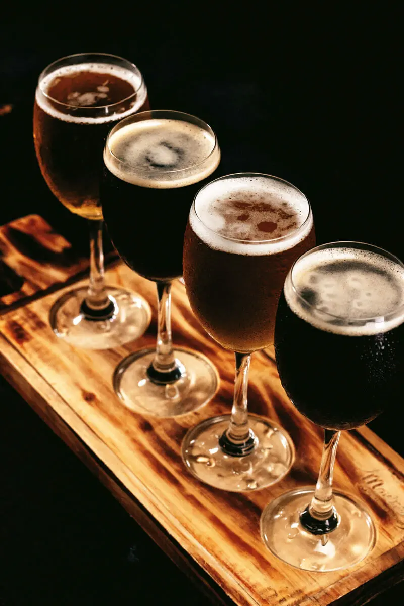 Vier Craft-Bier-Gläser auf Holzflight mit verschiedenen Biersorten in unterschiedlich dunkler Bierfarbe.