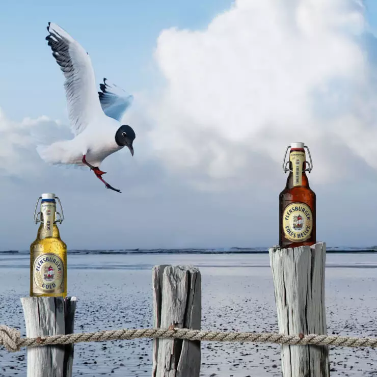 Vier Flensburger Flaschen stehen auf Holzstämmen am Meer.