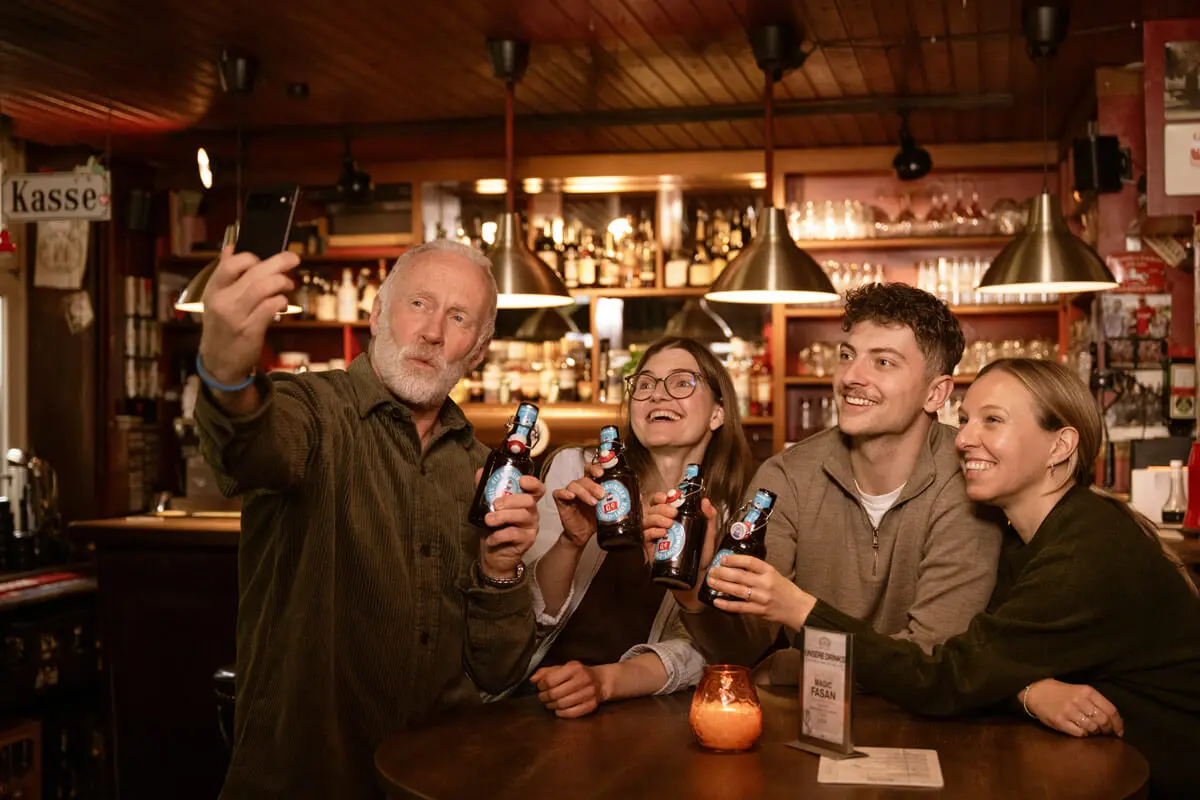 Gruppe von Leuten beim Selfie in rustikaler Bar, stoßen mit Flensburger Strand-Lager 0,0 % an.