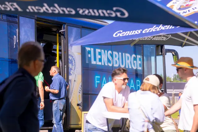 Einige Menschen stehen an Tischen, dahinter die Flensburger Fahrbar.