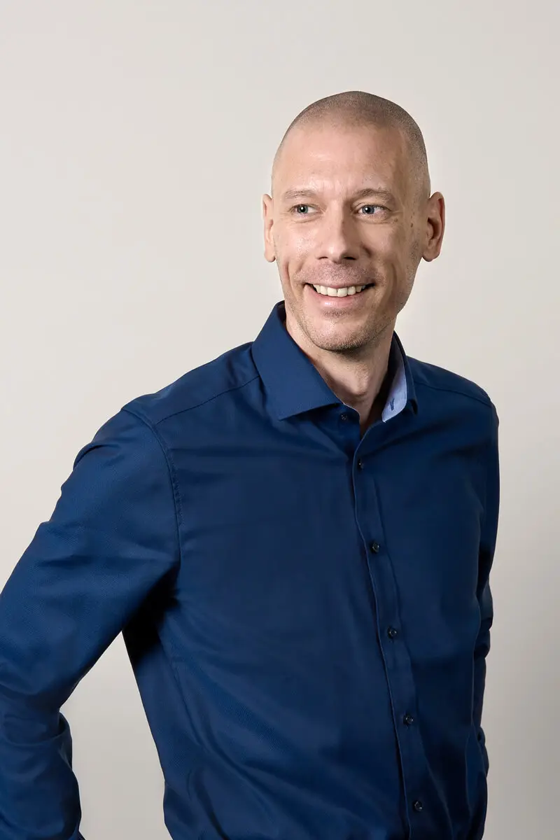 Porträt von Frank Wenig von Steinbeis in dunkelblauem Business-Hemd vor neutralem Hintergrund.