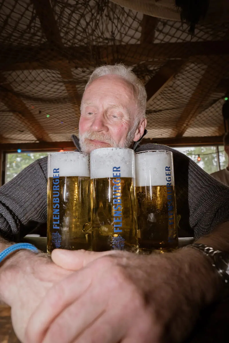 Andreas Arndt lächelnd hinter drei vollen Flensburger-Bierkrügen an einer Kneipentheke.