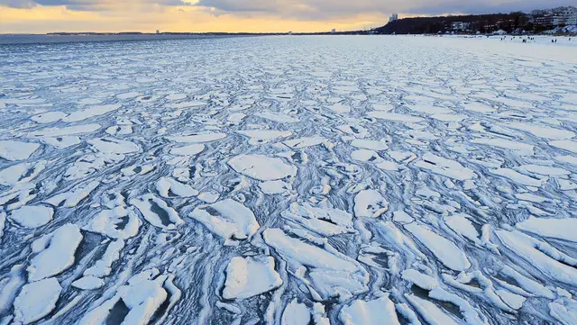 Vereiste Küste mit treibenden Eisschollen und Schneeschichten im Winter bei Sonnenuntergang.