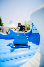 Junge surft auf einem blauen aufblasbaren Bullriding-Surfbrett bei der Kieler Woche 2025 am Küstenlimo-Stand.