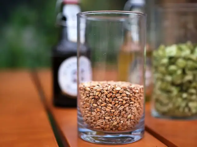 Ein Glas mit hellem Malz auf einem Holztisch, im Hintergrund eine Flensburger Bierflasche verschwommen.