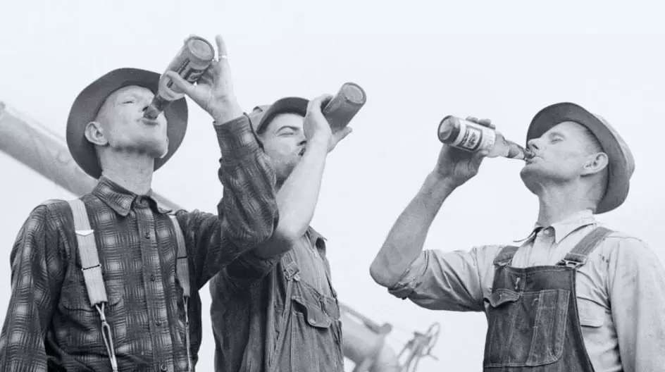 Historisches Bild dreier Männer, die aus Flensburger Bierflaschen trinken.