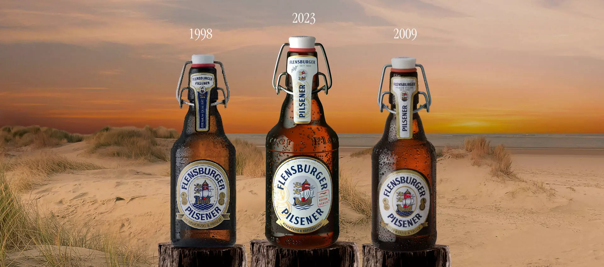 Drei Flaschen des Flensburger Pilseners stehen am Strand im Sonnenuntergang..
