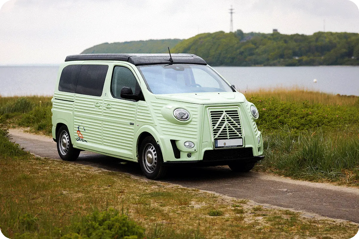 Mintgrüner Retro-Campervan am Küstenweg neben Stranddünen und Meer.
