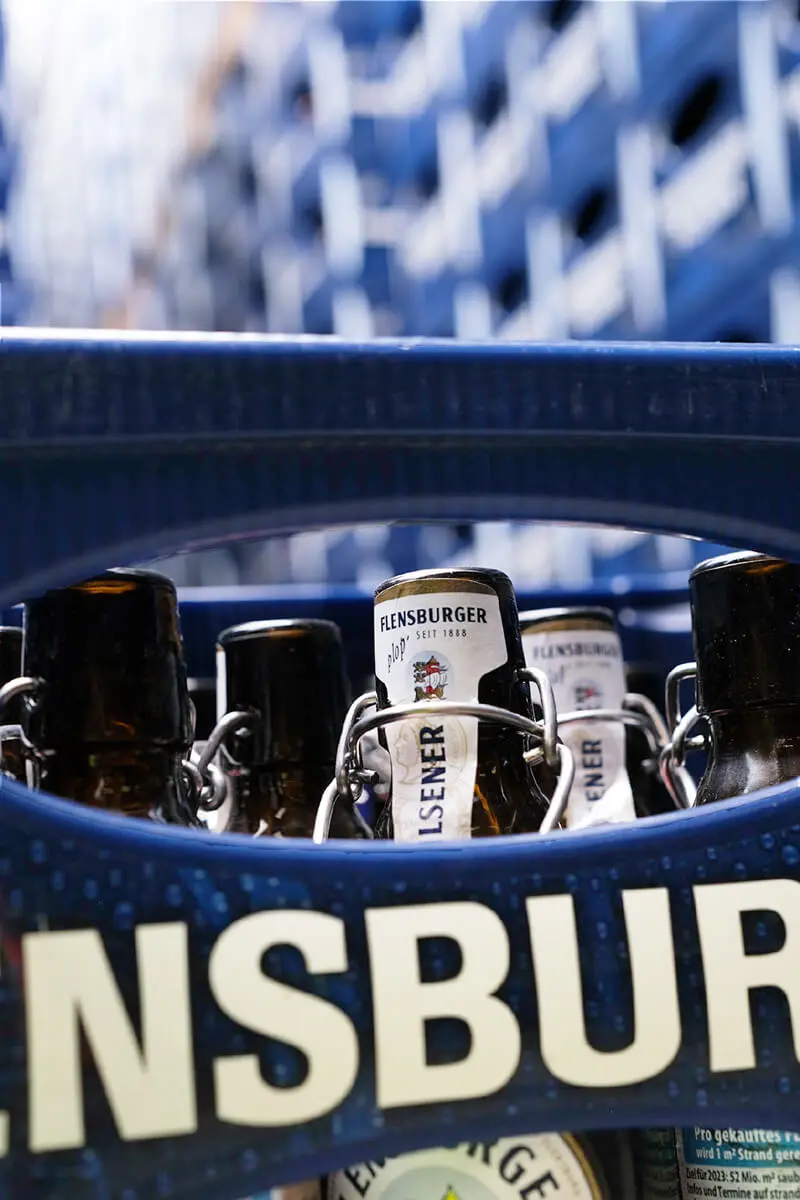 Flensburger Pilsener Bügelflaschen in blauer Bierkiste, Nahaufnahme der Etiketten und Flaschenhälse.