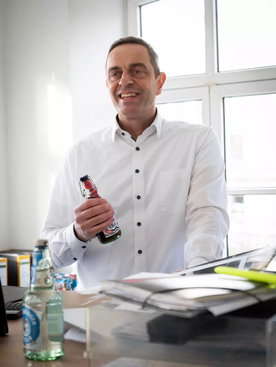 Ein Mann lächelt mit der Küstencola in der Hand in seinem Büro.