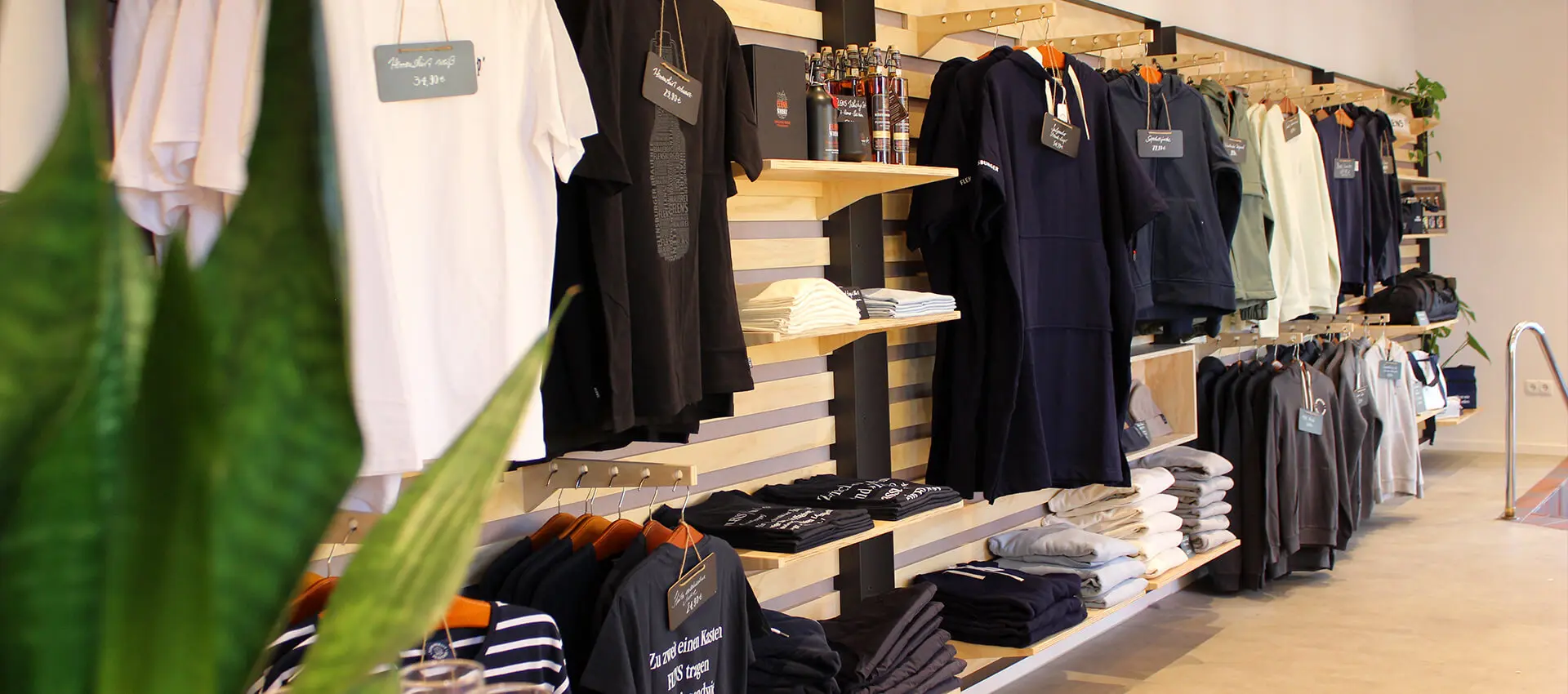 FLENS Klamotten und FLENS Merch an der holzverkleideten Wand im renovierten Plop-Shop.