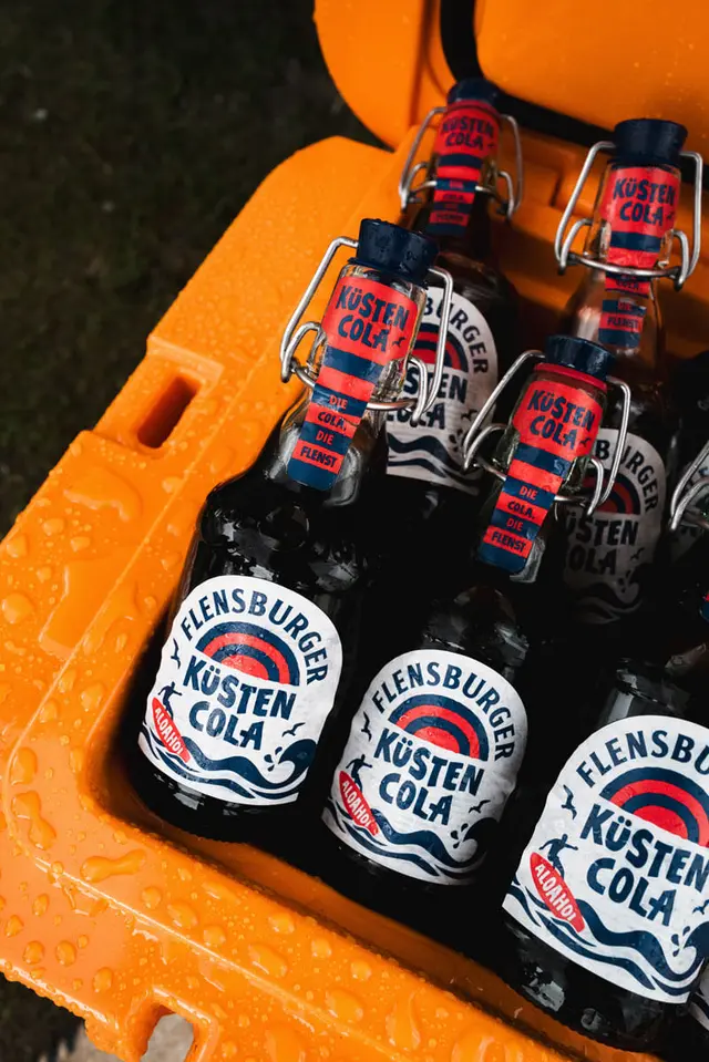 Flensburger-Küstencola-Glasflaschen im orangener Kühlkiste mit Wassertropfen.