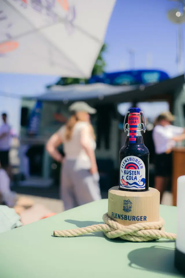 Flensburger-Küstencola-Flasche auf Holzsockel auf einem Sommerfest.