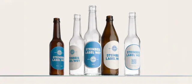 Fünf Glasflaschen mit blau-weißen Produktetiketten von Steinbeis.
