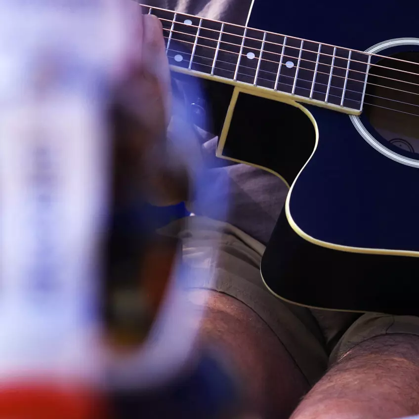Flasche Flensburger Pilsener vorne in der Unschärfe; im Hintergrund eine Hand, die Gitarre spielt.