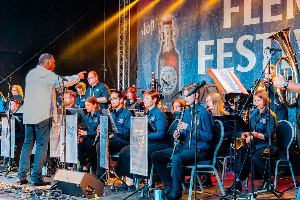 Der Dirigent dirigiert die lokale Big Band Flensburger Stadtbläser auf der Bühne des FLENS Festivals 2025.