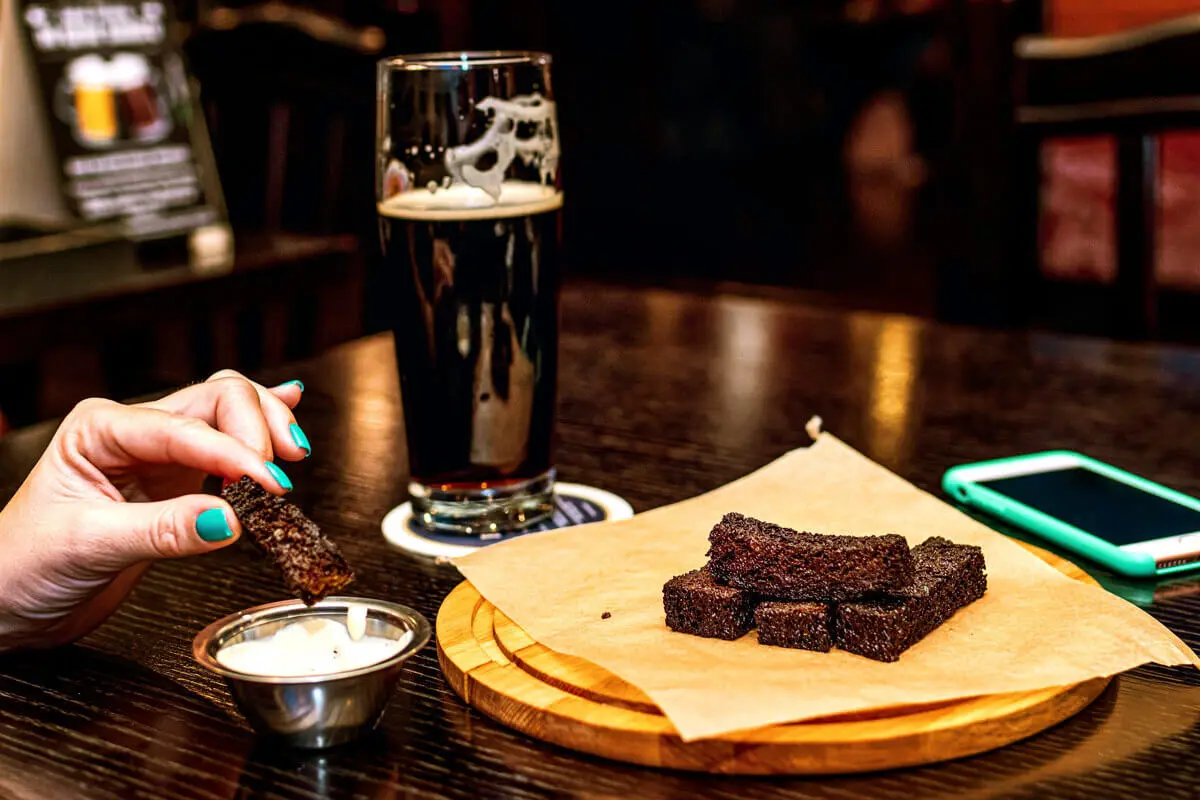 Hand dippt Schokoladenmüsliriegel, dahinter ein dunkles Bier im Pub.