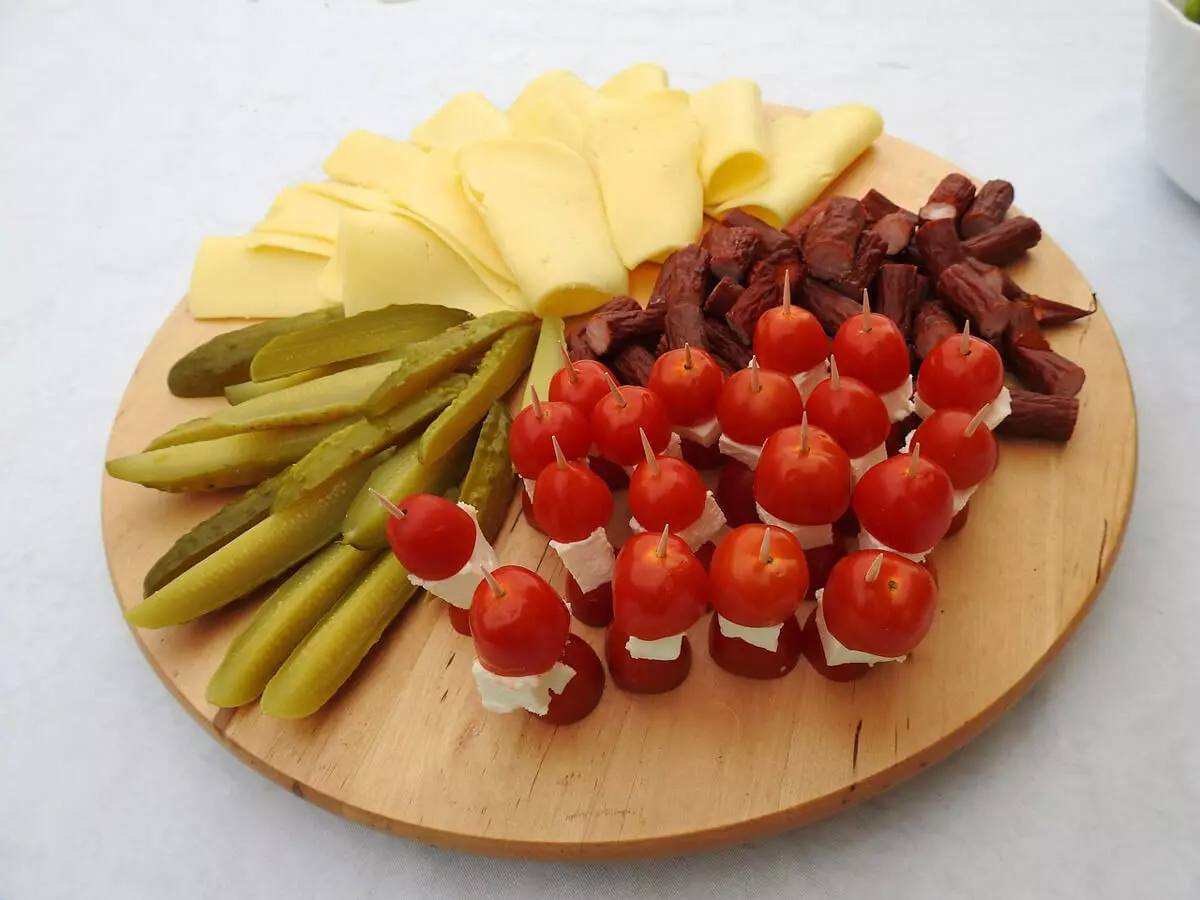 Ein Snackteller mit Käsescheiben, eingelegten Gurken, Tomatenhäppchen und Kabanossi.