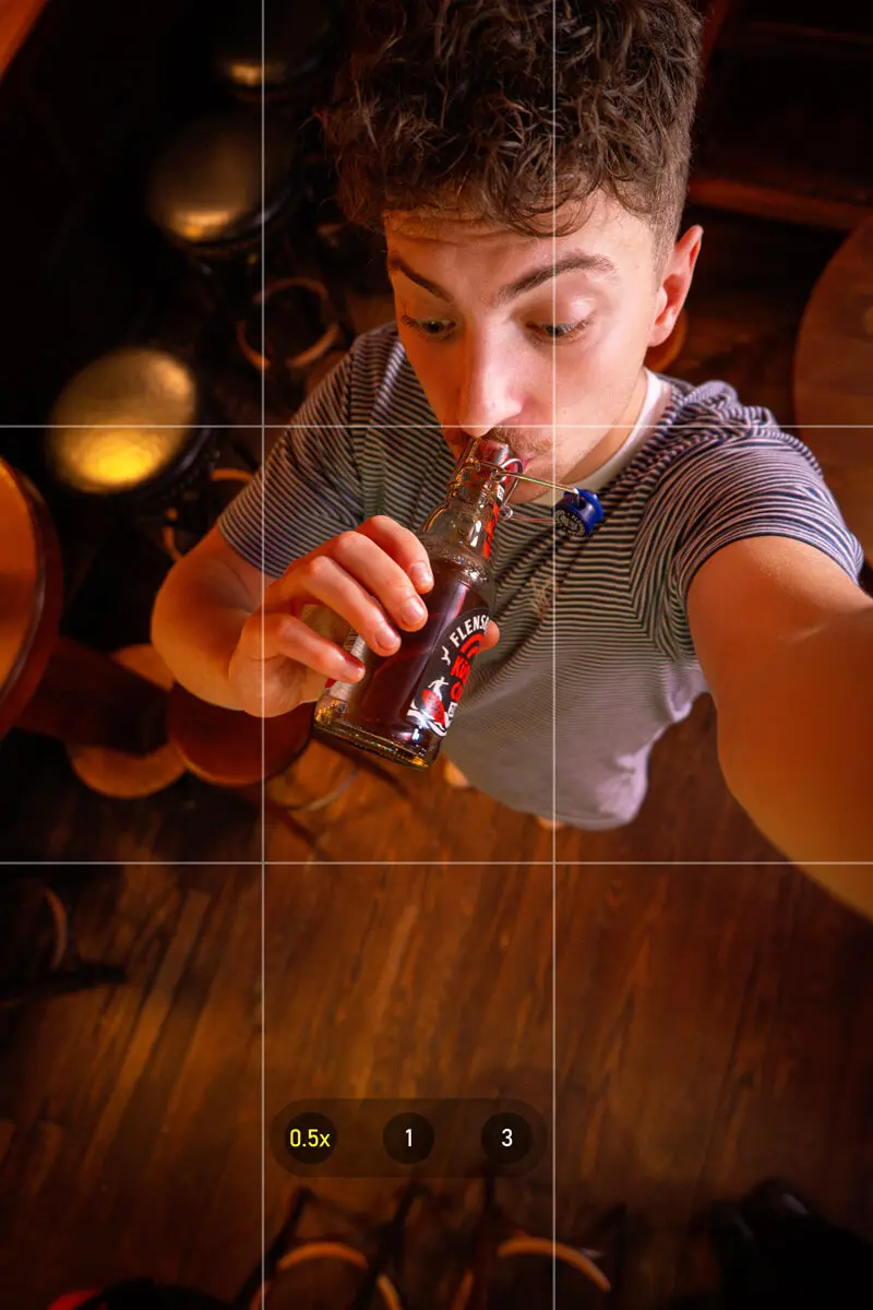 Junger Mann trinkt Flensburger Küstencola Zero aus einer Flasche in gemütlichem Raum, Selfie-Perspektive von oben.