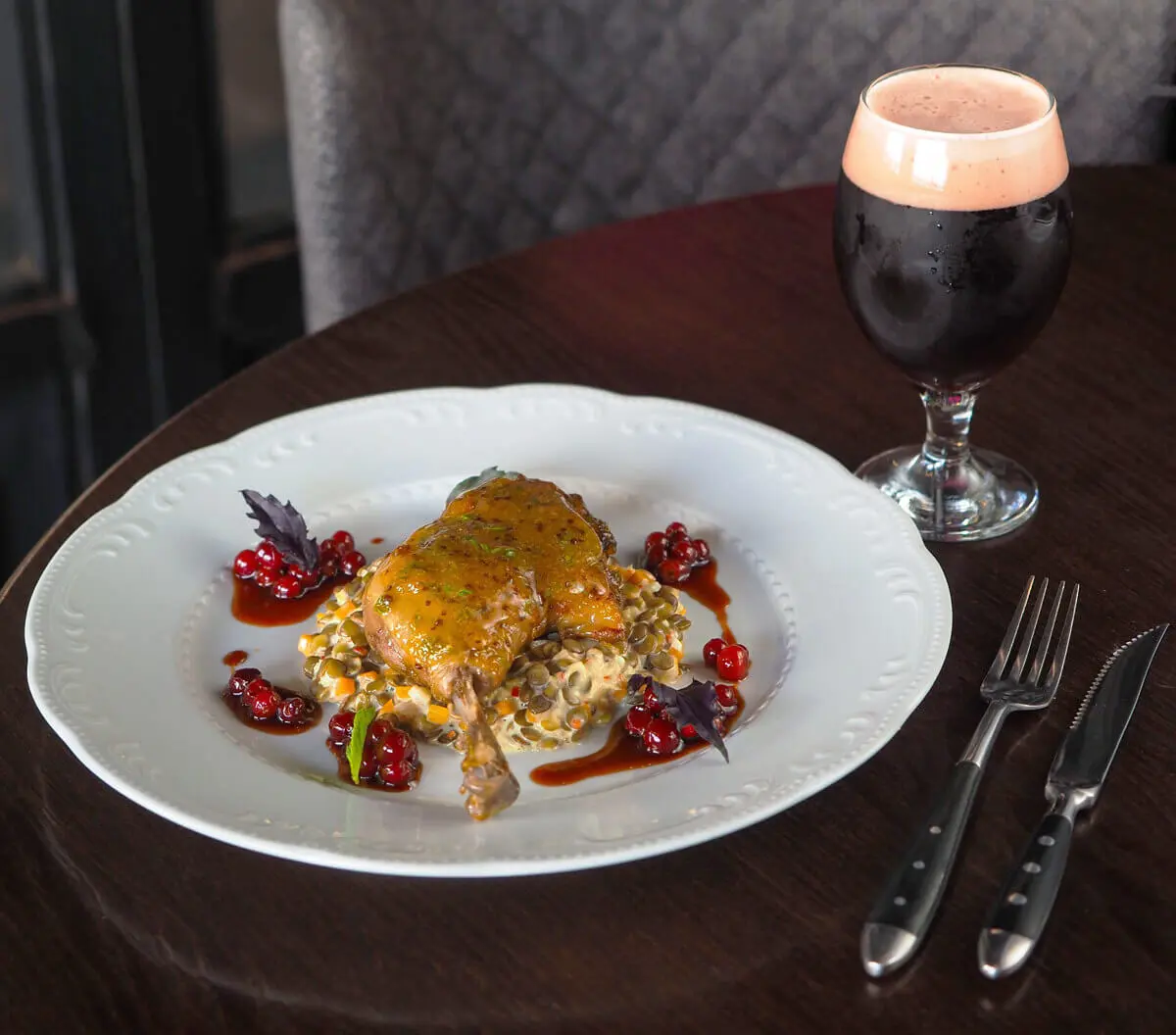 Entenkeule auf Linsengemüse mit Preiselbeeren, Dunkelbier und Soße auf weißem Teller.