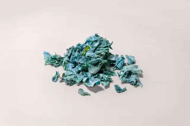 Haufen zerknitterter blau-grüner Papierfetzen auf hellem Hintergrund.