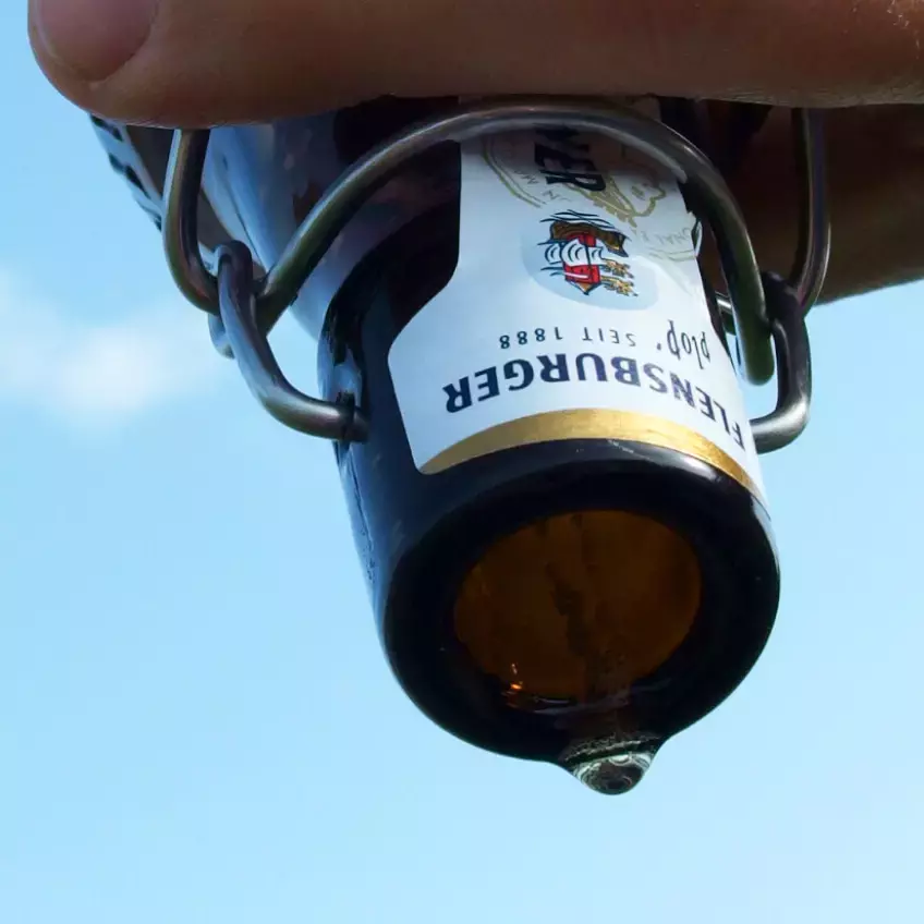 Offene Bierflasche, die von einer Hand über Kopf gehalten wird.