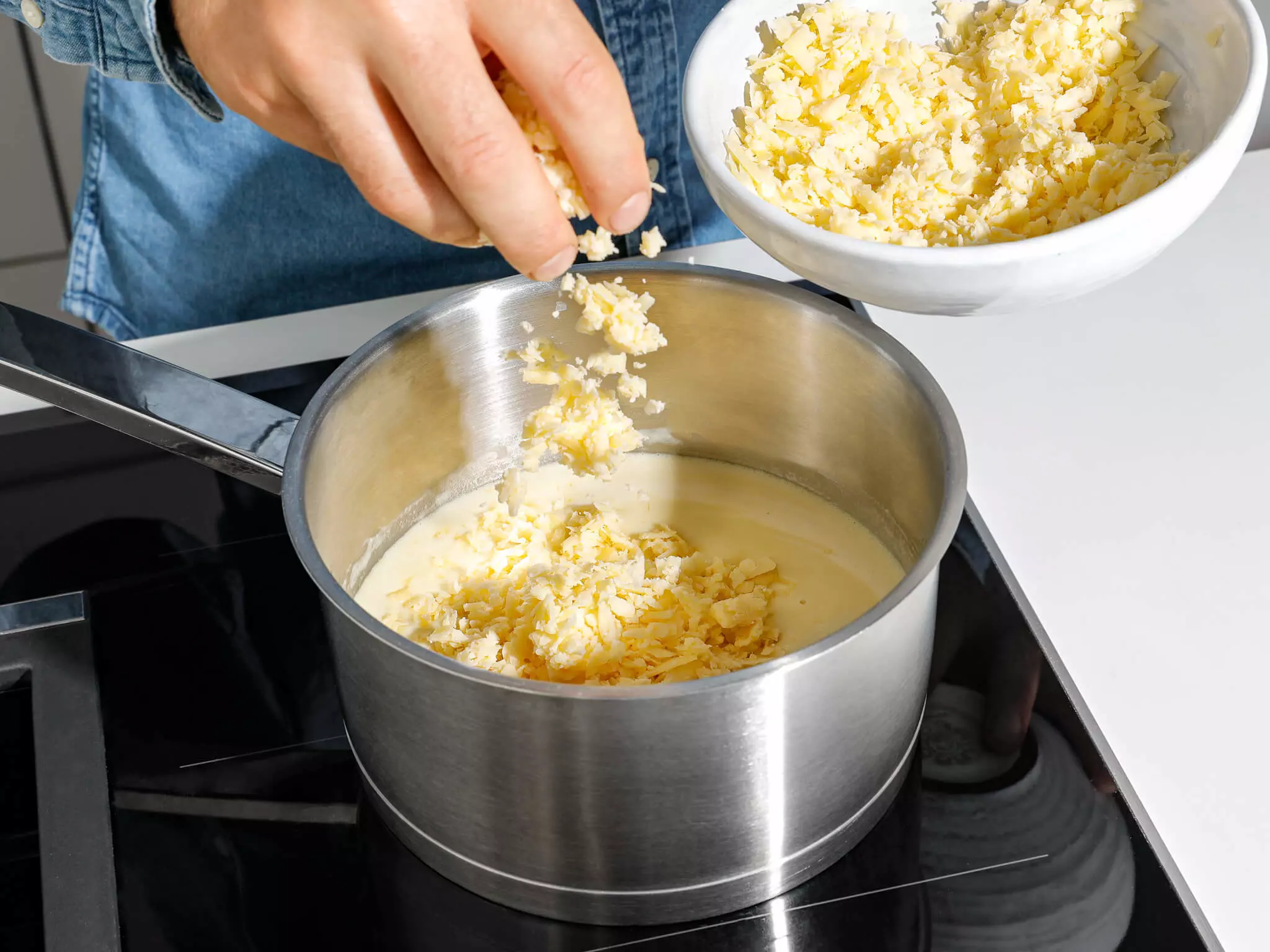 Geriebener Käse, der in einen Topf gestreut wird.