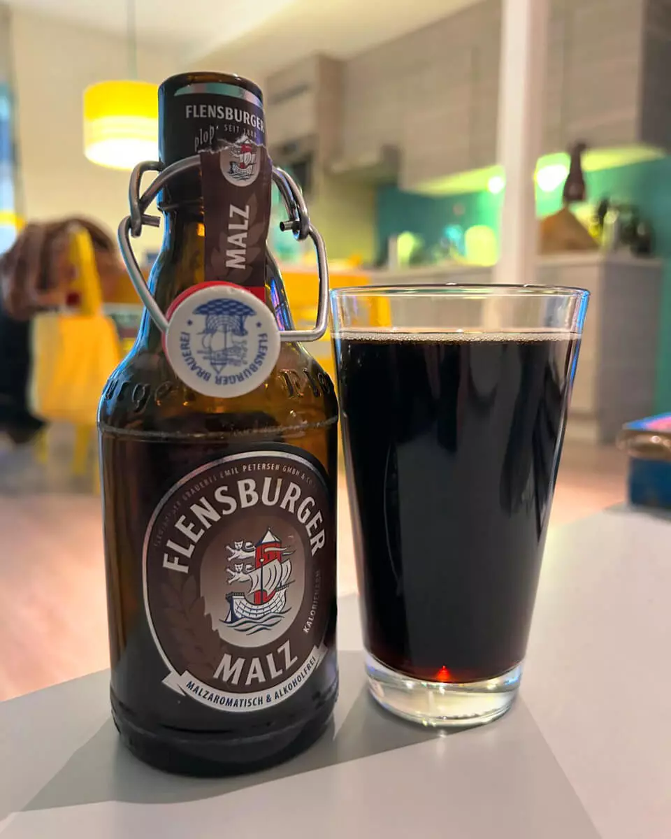 Eine Flasche Flensburger Malz steht geöffnet neben einem Glas, in dem der Malztrunk eingeschenkt wurde.