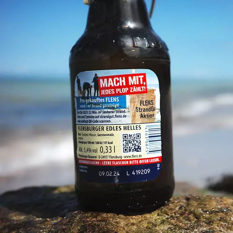 Rückenetikett mit MHD und Losnummer vom Flensburger Edles Helles auf Stein am Strand.