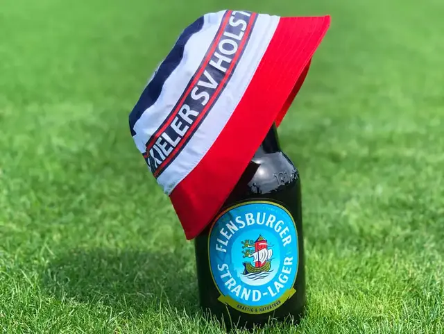 Mega-Plop Strand-Lager mit Holstein-Kiel-Anglerhut steht auf dem Stadionrasen.