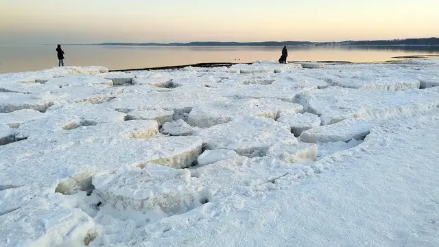 Vereiste Küste mit Eisschollen und Personen, ruhiges Meer bei Winterdämmerung.