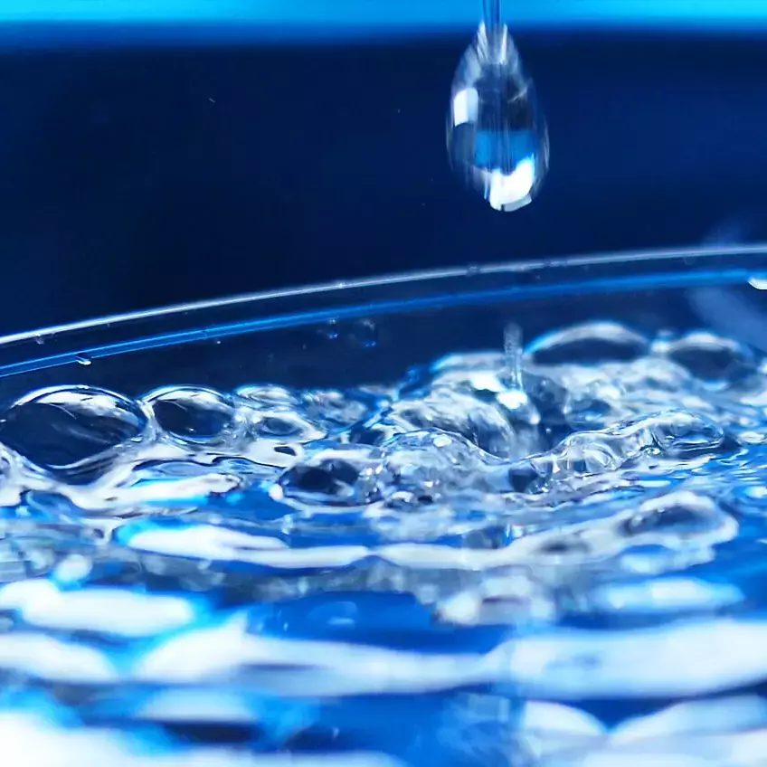 Wasser in einem Glasgefäß, auf die Oberfläche fällt ein Tropfen.