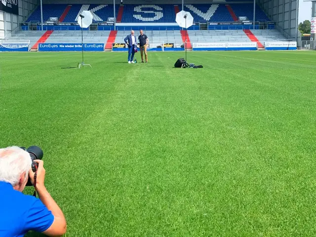 Fotograf liegt auf dem Stadionrasen im Holstein-Stadion und fotografiert die Geschäftsführer vom KSV und FLENS.