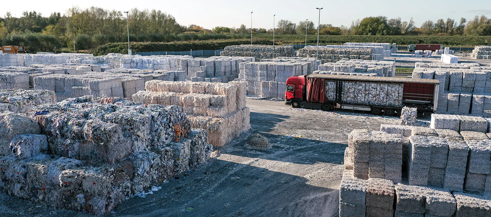 Altpapier-Recyclinghof mit gestapelten Papierballen und rotem LKW bei Steinbeis.