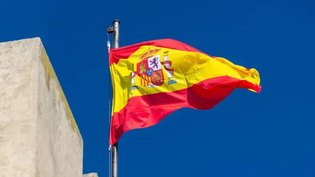 Die gehisste Flagge Spaniens vor blauem Himmel.