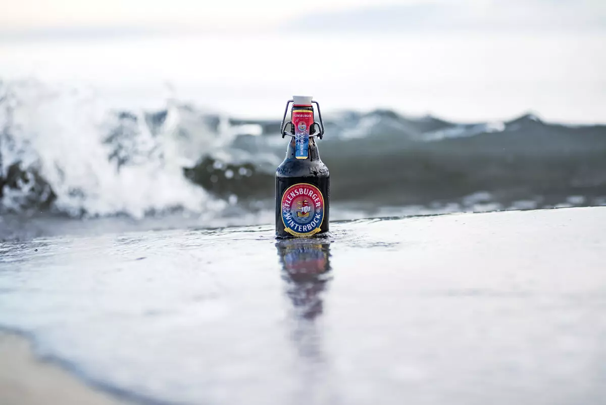 Eine einzelne Flasche Flensburger Winterbock in der Welle am Strand.