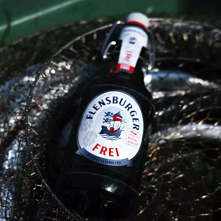 Eine Flasche Flensburger Frei in einem Fischernetz auf einem grünen Boot.