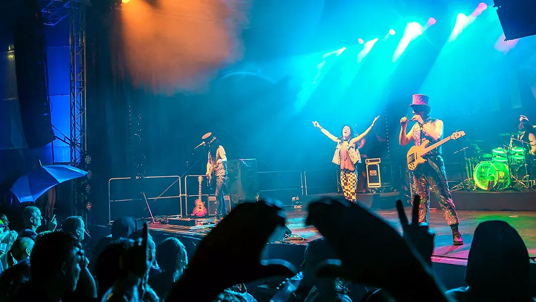 Die Coverband "Hit Radio Show" beim FLENS Festival 2023 auf der Bühne; im Vordergrund Publikumshände, die ein Herz bilden.