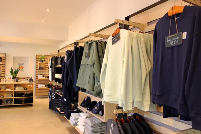 Etliche FLENS Klamotten an der schicken, holzverkleideten Wand im renovierten Plop-Shop.