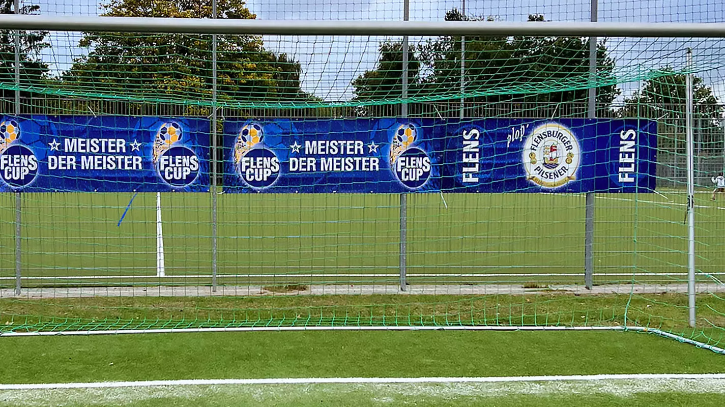 Blaue FLENS Bandenwerbung hinter einem Fußballtor.